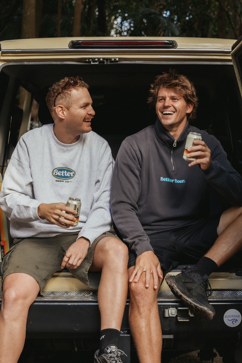 Two men sitting in the back of a car, enjoying drinks together in their better beer crew necks.